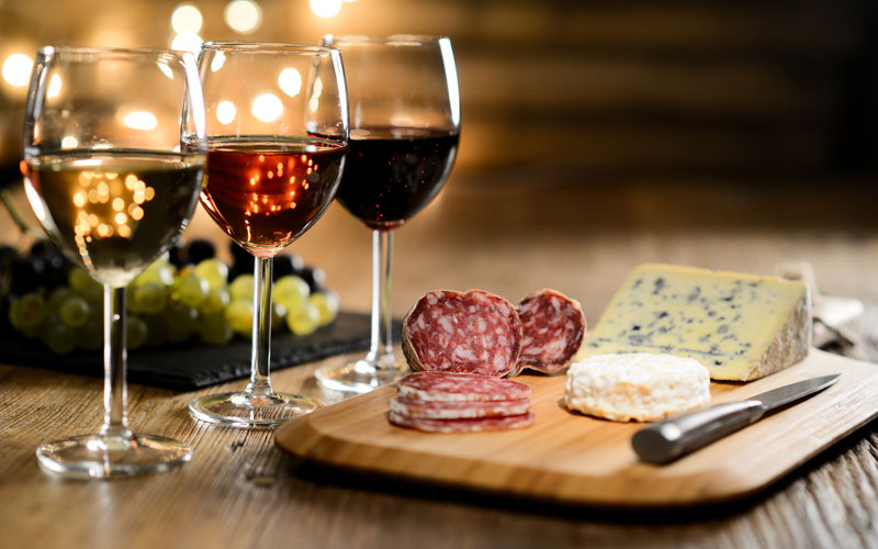 Three Glass Of Red Wine, Rose Wine And White Wine With French Cheese And Delicatessen In A Restaurant Wooden Table With Romantic Dim Light Cosy Atmosphere